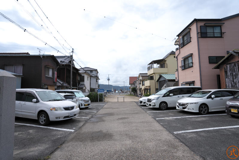 正面（南）を望む。駐車場の先の土の部分の終わりあたりがかつての海岸だったと思われる。ちなみにこの駐車場は月極なので注意されたし。